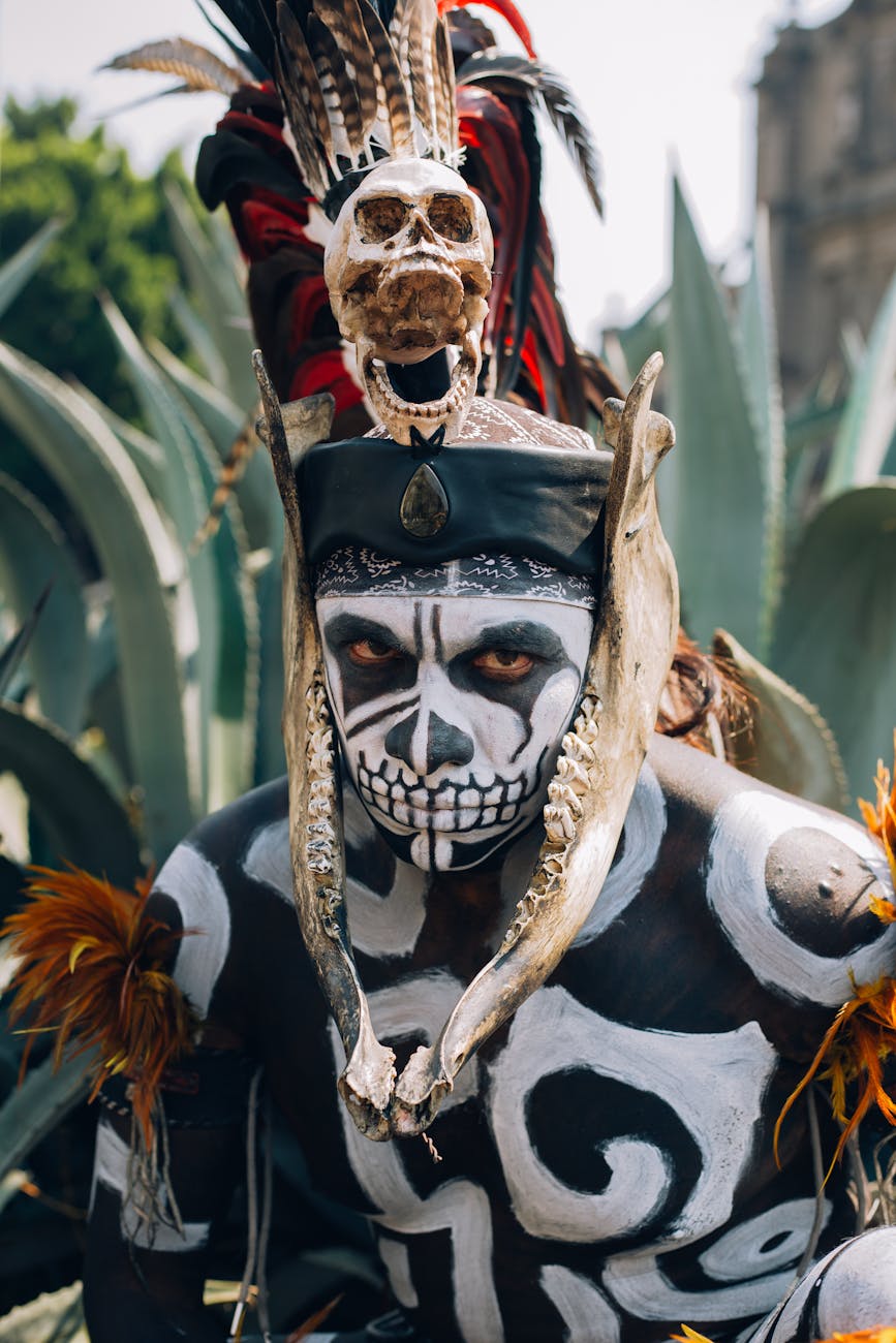 native mexican aztec warrior with pre hispanic makeup simulating a skull and a bone headdress adorned with feathers and cempazuchil flowers