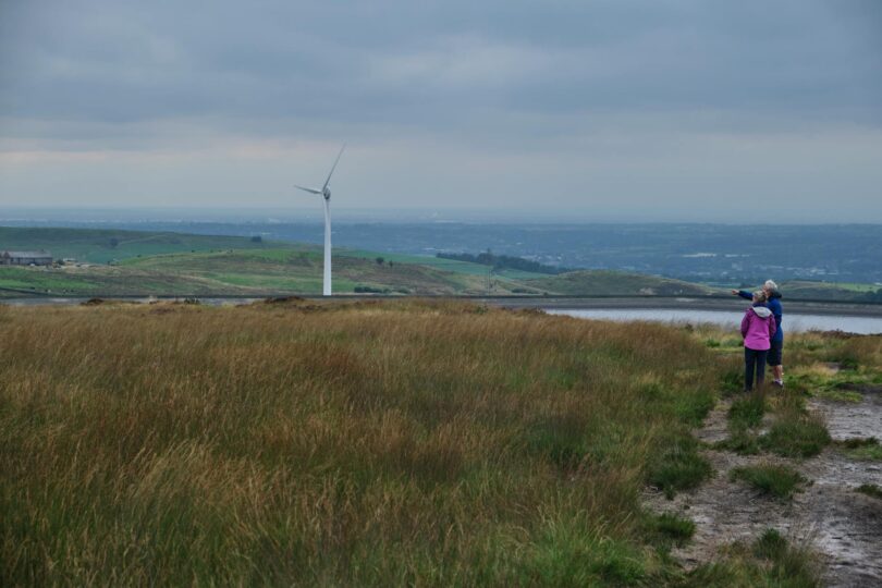 anonymous female travelers looking at windmill in meadow in countryside